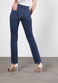 Jeans de mezclilla azul oscuro con corte slim, cinco bolsillos y costuras en contraste. Combinados con zapatos de tacón alto en blanco y negro.