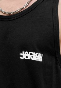 Crni pamučni top bez rukava s bijelim logom "JACK & JONES". Okrugli izrez i fine rebraste ivice. Uključuje srebrni lančić kao dodatak.