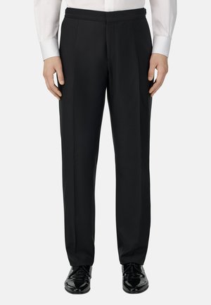 Czarne eleganckie spodnie o smukłym kroju, z płaskim przodem i prostymi nogawkami, wykonane z gładkiego materiału. W zestawieniu z wypastowanymi czarnymi butami.