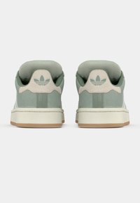 Green suede sneakers with a white rubber sole, featuring a textured surface and a beige accent on the heel with a trefoil logo.