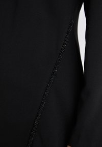 Mustmust koos elegantse sileda kanga ja tekstuuriga helkivate detailidega külje ääres, mis lisab kogu disainile õrna ilu.