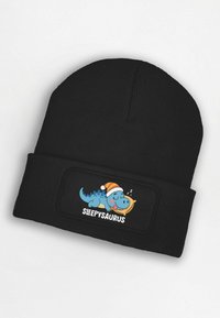 Black knit beanie featuring a stitched patch with a blue cartoon dinosaur sleeping, wearing a Santa hat, and holding a banana. Text: "SLEEPSAURUS."