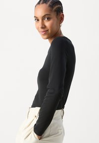 Svart topp med lange ermer laget av myk stoff, med en tettsittende design. Parret med lyse høyt midjefede bukser. Minimalistisk stil.