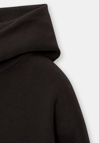 Gros plan d'un sweat à capuche noir montrant la capuche pliée et la couture de l'épaule sur un fond clair.