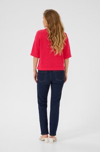 Rosa gestricktes Kurzarm-Oberteil, kombiniert mit dunklen Jeans. Das Oberteil hat einen strukturierten Stoff, einen lässigen Schnitt und eine gerade Passform.