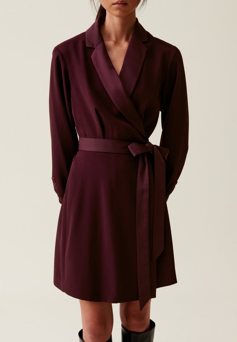 Vestido envolvente burdeos con mangas largas, cuello chal y un cinturón a juego atado en la cintura. Tejido suave, hasta la rodilla, con un detalle mínimo.