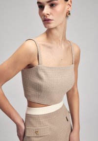 Beige gequoteerde crop top met dunne bandjes, met een vierkante halslijn. Draag het met een hooggewaisted rok met een crèmekleurige tailleband en zijkonijn.