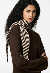 Écharpe tricotée à rayures beige et brun foncé, avec une texture douce et de longues extrémités ondulées, posée sur un vêtement brun foncé.