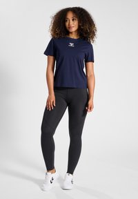 Marineblauwe T-shirt met korte mouwen en een wit logo, gecombineerd met zwarte leggings met een textuurdesign en witte sportieve sneakers.