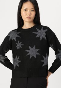 Black sweater with silver star patterns, made of textured fabric. Features a round neckline and ribbed hem and cuffs.