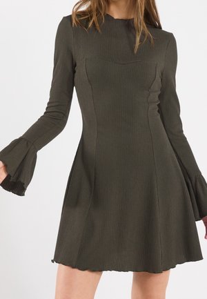 Abito verde scuro, con texture, maniche a campana lunghe e corpino aderente. Presenta un orlo smerlato e una silhouette a linea ad A.