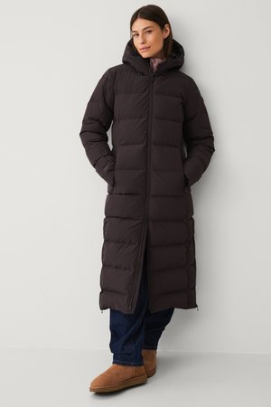 Lange, donkerbruine pufferjas met een ritssluiting aan de voorkant, kap en geborduurde design. Gekocht met blauwe spijkerbroeken en tan suède laarzen.