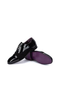 Zapatos de vestir de charol negro con punta de ante, diseño con cordones y plantilla morada con suela lisa.