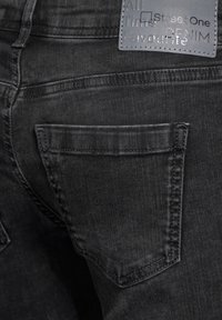 Černé džíny z denimu s dvěma zadními kapsami, prošívaným švem a šedou značkovou visačkou s vyraženým písmem.