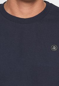 Ciemnoniebieska bawełniana koszulka z okrągłym dekoltem i krótkimi rękawami, z okrągłym logo z małą literą "a" na klatce piersiowej.