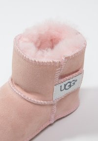 Rosa Wildleder-Ankle-Boot mit weichem rosa Fleecefutter, sichtbaren Nähten und einem UGG-Logo-Patch an der Seite. Kurz geschnittenes Design.