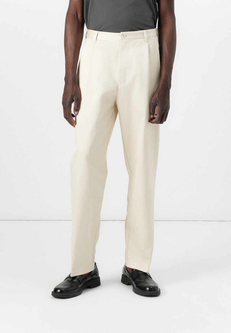 Pantalon beige à coupe droite, avec fermeture à bouton, passants de ceinture et poches avant. Le tissu est lisse et léger.
