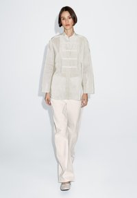 Jasnozielona koszula z długim rękawem, ozdobiona pionowymi paskami i kołnierzykiem typu mandarynka, zestawiona z luźnymi kremowymi spodniami oraz płaskim obuwiem.