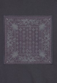 Dark fabric with a square graphic print featuring light gray floral and geometric patterns, bordered by an illustrated design and text.