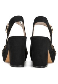 Tacones de plataforma de ante negro con amplios cortes y una correa ajustable para el tobillo. Los tacones en forma de cuadrado ofrecen un soporte estable.