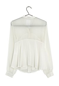 Vit långärmad blus i genomskinligt tyg, med plisserad design vid midjan, rundad nederkant och knäppta ärmslut. Hänger på en krok.