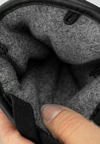 Pochette noire avec un intérieur en feutre gris doux. Présente une finition texturée et un doigt touchant l'ouverture, mettant en avant la douceur de la doublure.
