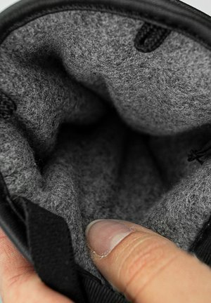 Borsa nera con un morbido interno in feltro grigio. Presenta una finitura testurizzata e un dito che tocca l'apertura, evidenziando la morbidezza della fodera.