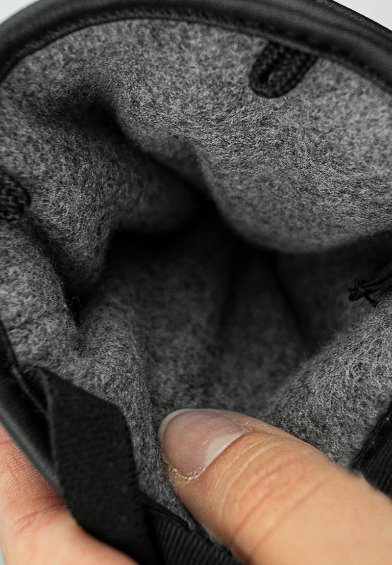 Sort pouch med blødt gråt filt indvendigt. Har en tekstureret overflade og en finger, der rører ved åbningen, hvilket viser indretningens blødhed.
