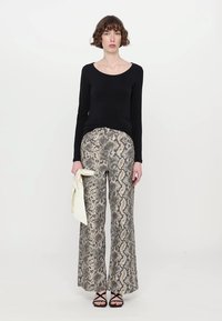 Zwarte lange mouwen top gecombineerd met brede, slangenprints broek in beige en grijs. Inclusief een licht crèmekleurige sjaal als accessoire.