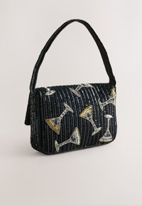 Sac à main noir perlé avec une bandoulière courbe, décoré de motifs de verres à cocktail dorés et argentés, et une surface texturée en sequins.