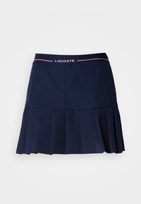 Jupe plissée bleu marine avec ceinture élastique ornée du logo Lacoste et de fines rayures roses sur fond blanc.