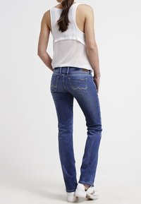 Denimjeans i en medelblå tvätt med rak passform och subtila sömmar på bakfickorna. Bärs med en genomskinlig vit topp och vita sandaler.