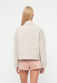 Veste en velours côtelé beige clair avec un col court, des épaules tombantes et des poignets élastiques. Associée à un short en daim rose.