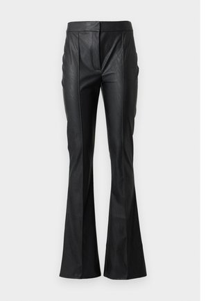 Jeune femme aux longs cheveux foncés porte un blazer en cuir vert foncé et un pantalon, un pull col en V beige et des sandales à talons noires.
