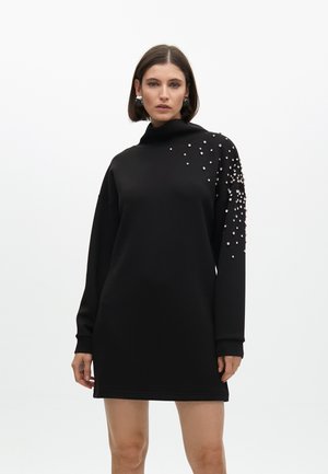 Black sweatshirt dress with a high collar, long sleeves, and scattered pearl embellishments on one shoulder. Smooth fabric, relaxed fit.