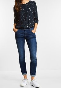 Mörkblå blus med vita prickar, rund halsringning, trekvartslånga ärmar. Matchas med medelintensiva skinny jeans och vita sneakers.