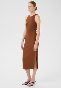 Abito midi marrone a coste, senza maniche, con uno spacco laterale e una silhouette aderente. Abbinato a ciabatte nere. Design minimalista.