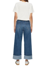 Brede denim jeans met een medium wassing, voorzien van opgerolde mouwen en achterzakken. Gepaard met een plain witte T-shirt met korte mouwen.