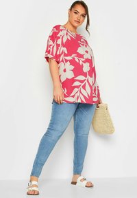 Top rosa con stampa floreale e maniche corte, abbinato a jeans skinny azzurri. Accessoriato con una borsa intrecciata e sandali bianchi.