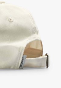 Witte katoenen baseballpet met een gebogen klep, voorzien van een metalen verstelbare strap en een merketiket aan de zijkant. Gladde textuur.