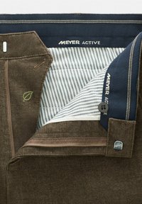 Bruine stoffen broek met een blauw gestreepte voering. Kenmerken zijn een rits, een knoop en groene bladeren borduurwerk. Merknnaam "MEYER ACTIVE" zichtbaar.