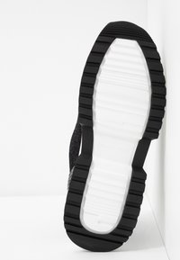 Semelle en caoutchouc noire à texture rainurée, dotée d'une semelle intermédiaire blanche. Le design présente un bord incliné et une finition noire lisse.