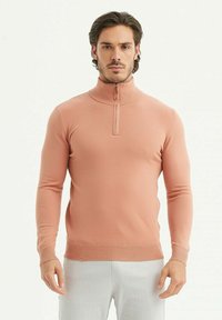 Pull à col zippé rose clair en tissu côtelé ; il présente des manches longues et un design ajusté avec une texture subtile.