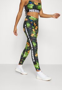 Czarny crop top i legginsy w tropikalny kwiatowy wzór, z liściastymi motywami i białymi akcentami z logo. Białe buty sportowe.