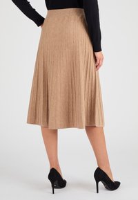 Gonna plissettata color beige realizzata in tessuto testurizzato, con una cintura larga. Abbinata a scarpe nere con tacco alto, che aggiungono contrasto all'outfit.
