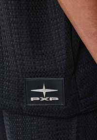 Zwarte gestructureerde stof met een geweven patroon; bevat een rechthoekig zwart label met zilveren "PXP" logo en een sterembleem.