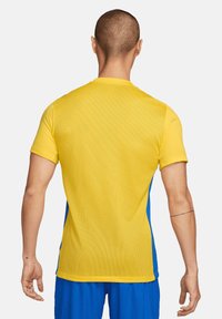Maglia sportiva con parte superiore gialla e lati blu, realizzata in tessuto in rete. Presenta un colletto tondo e maniche corte, accentuando la traspirabilità.