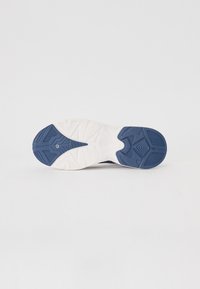 Semelle de chaussure de sport avec un grip texturé en caoutchouc blanc et bleu, présentée à plat sur un fond clair uni.