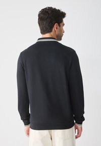 Sort sweatshirt med krave, prydet med hvide striber. Glat tekstur og afslappet pasform, med lange ærmer og lige kant.