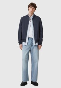 Mornarska bomber jakna čez svetlo modro srajco z gumbi, v kombinaciji s svetlo opranimi jeans hlačami s pravimi hlačnicami in črnimi škornji. Preprost dizajn, vsakdanji videz.